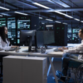 Person with paraplegia and colleague working in inclusive server hub workspace, typing on PC. Man in wheelchair and coworker doing tasks in data center housing advanced data storage infrastructure